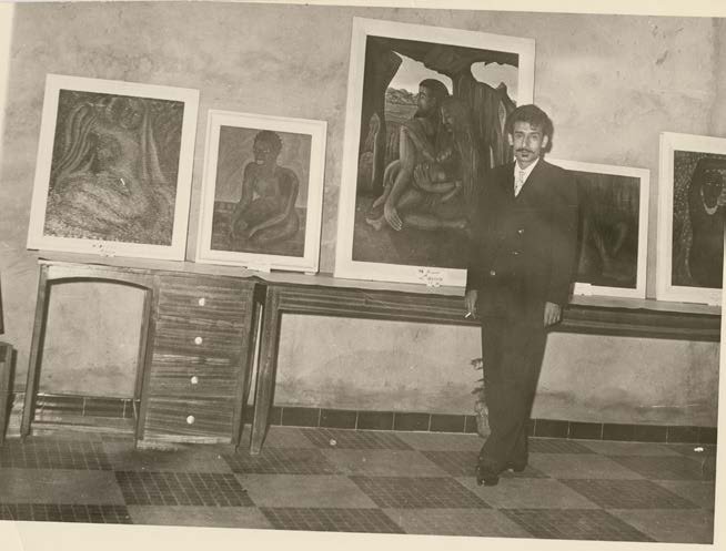 Aref El Rayess standing beside a wall of his portrait paintings